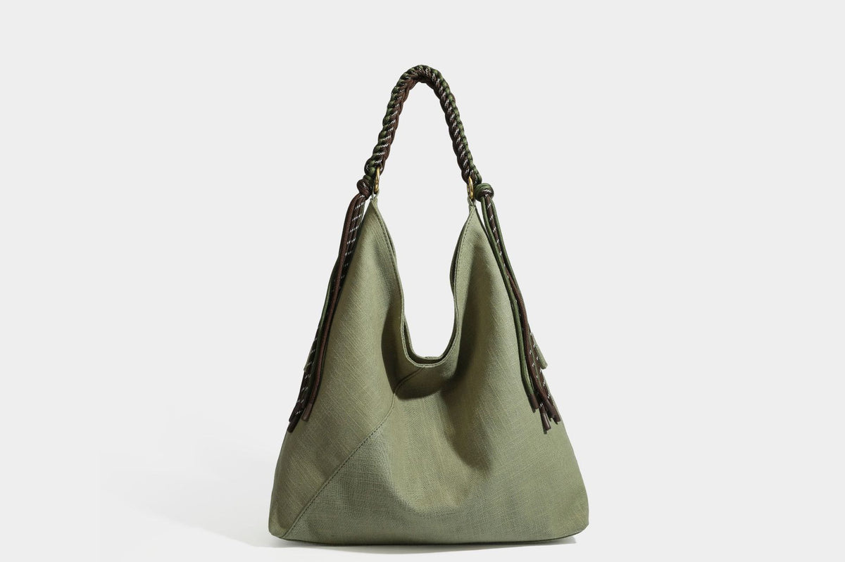 Soft slouchy cream canvas shoulder tote with braided brown and green cord handle, gold-tone ring hardware, and tassel trim