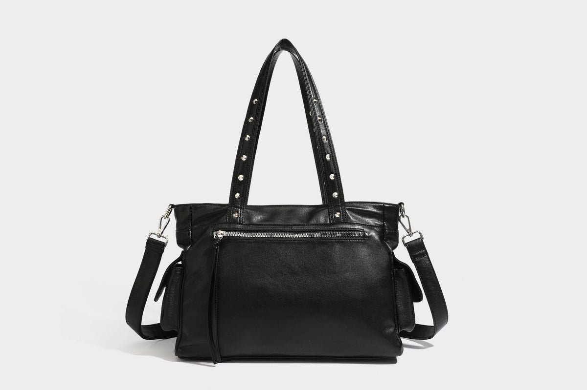 Black leather-look tote bag with silver pyramid studs on handles and front panel, multiple flap and zip exterior pockets