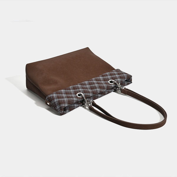 Brown structured tote bag with woven plaid fold-over top panel, silver-tone ring hardware, and long flat shoulder straps