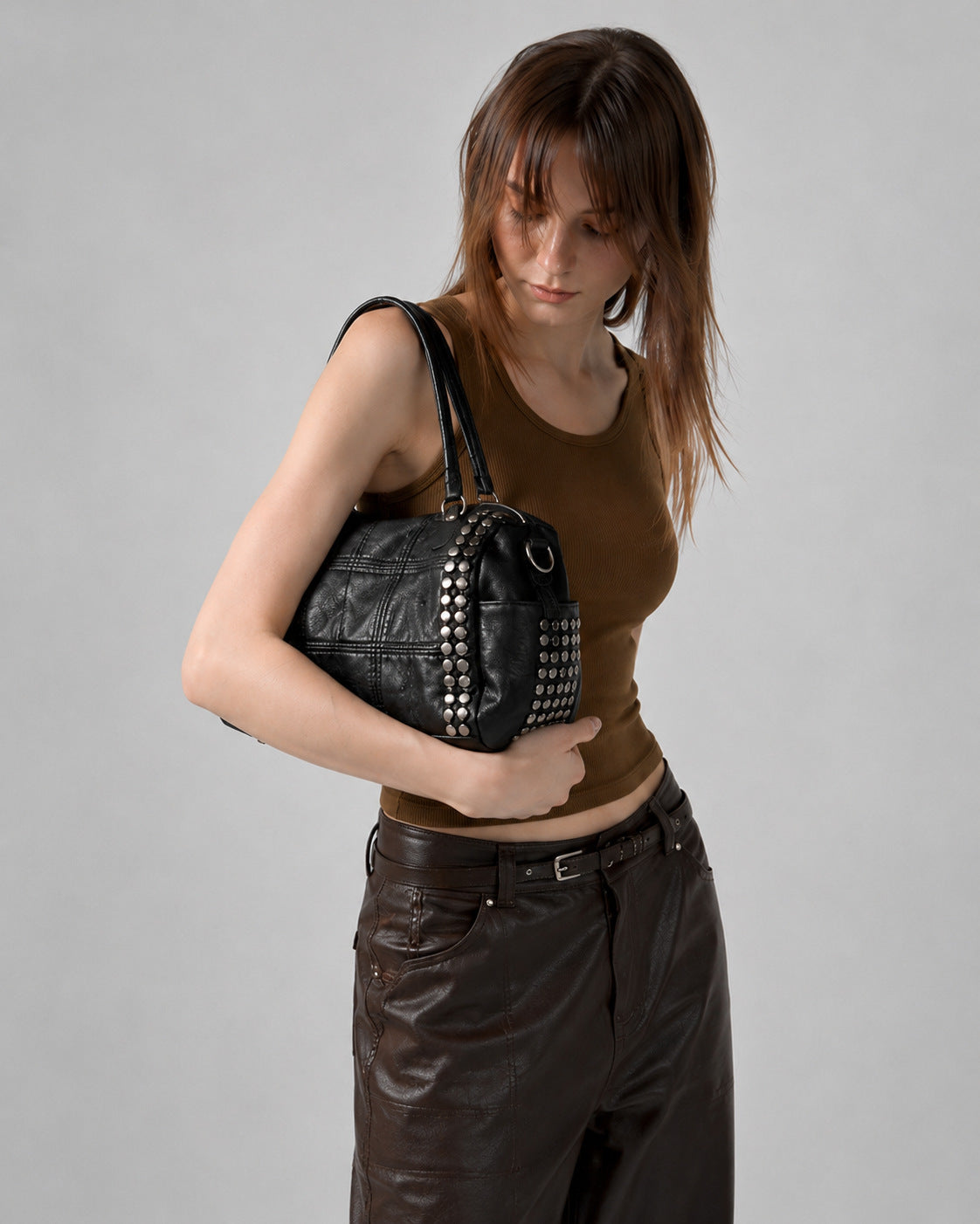 Black leather-look satchel bag with gunmetal rivet trim, grid-stitched paneling, dual rolled top handles, and curved zip