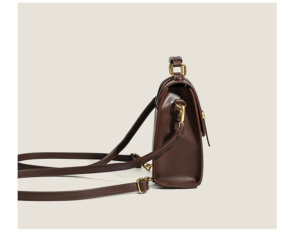 Structured mini satchel backpack with smooth leather-look finish, front flap pocket, gold-tone stud closures, and top handle