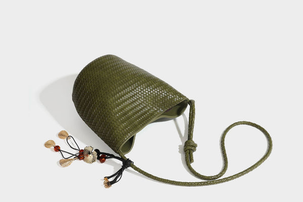Olive green woven leather-look bucket bag with braided crossbody strap, knotted adjustment, and gold-tone tassel charm with