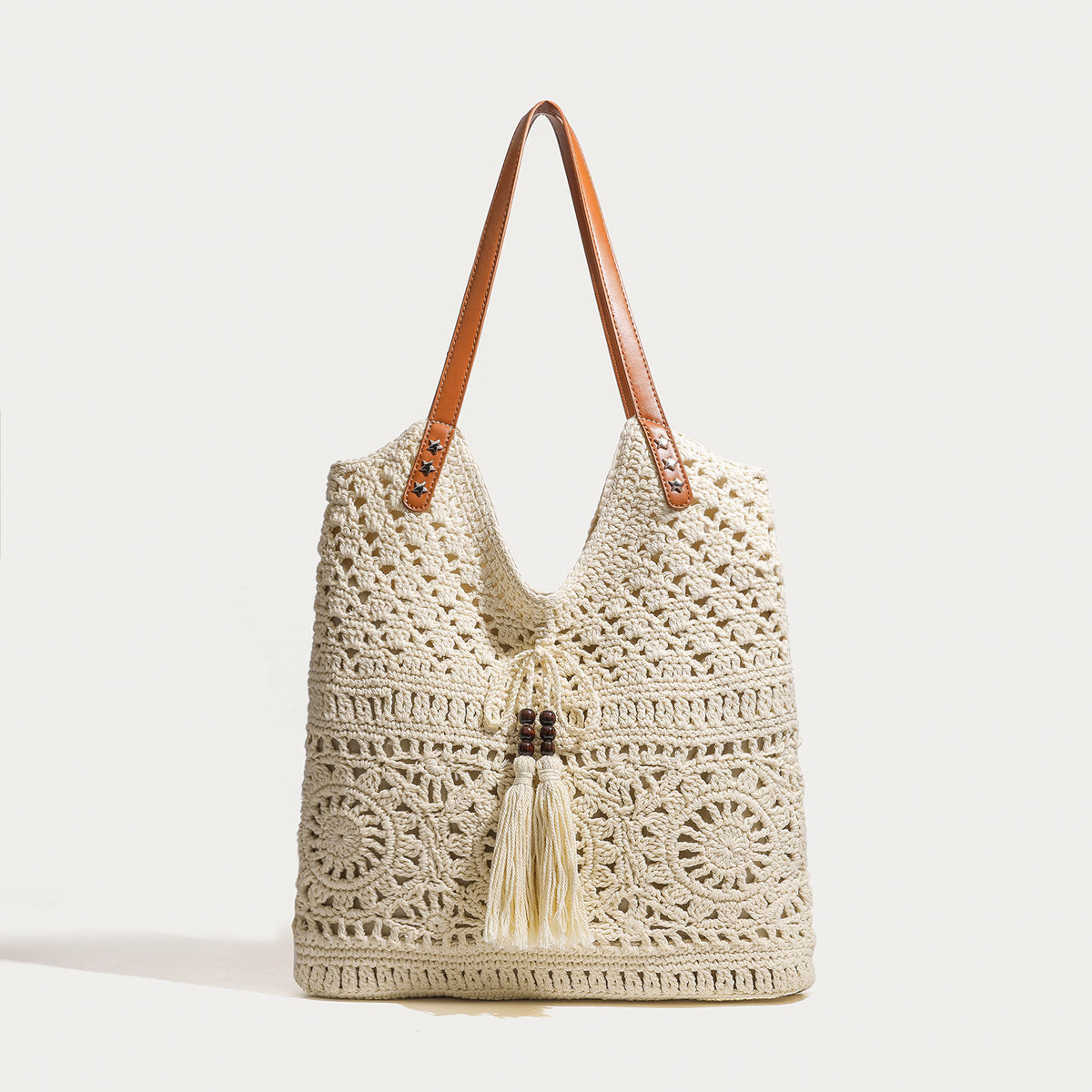 Cream openwork crochet tote bag with tan leather-look double shoulder straps and tassel drawstring tie, detail view 6