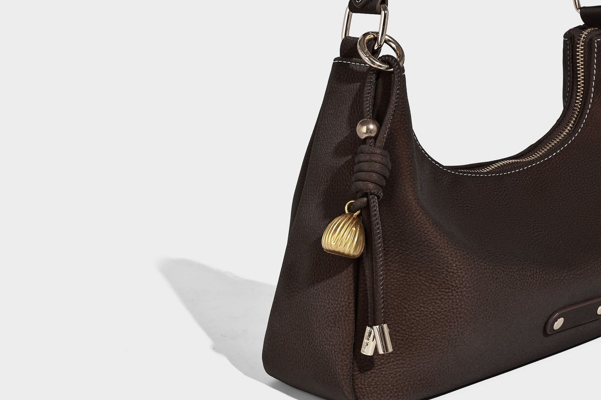 Crescent hobo shoulder bag in pebbled leather-look finish with top zipper, adjustable strap, gold-tone ring hardware, and