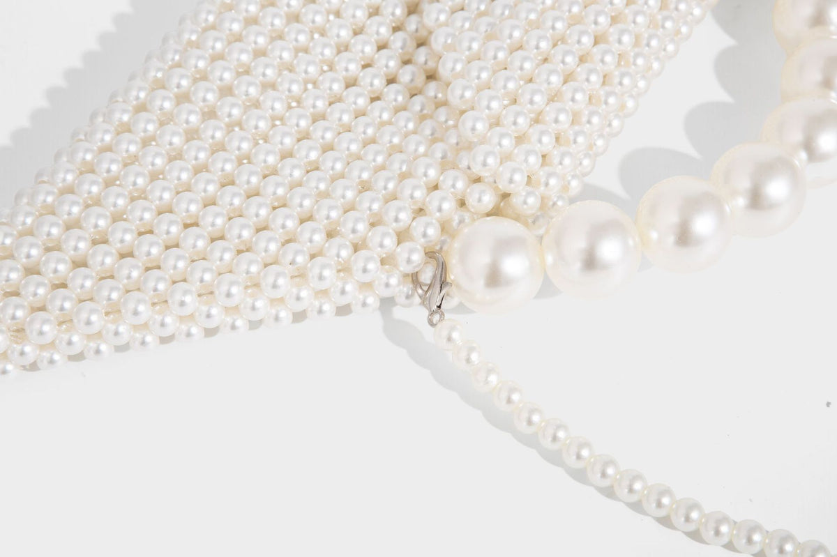 Small structured triangle clutch bag covered in glossy pearl beads with an arched pearl top handle and silver snap closure