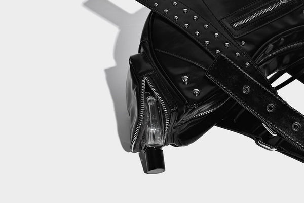 Glossy black crescent shoulder bag with silver-tone rivets, multiple zip pockets, and long adjustable studded straps, detail