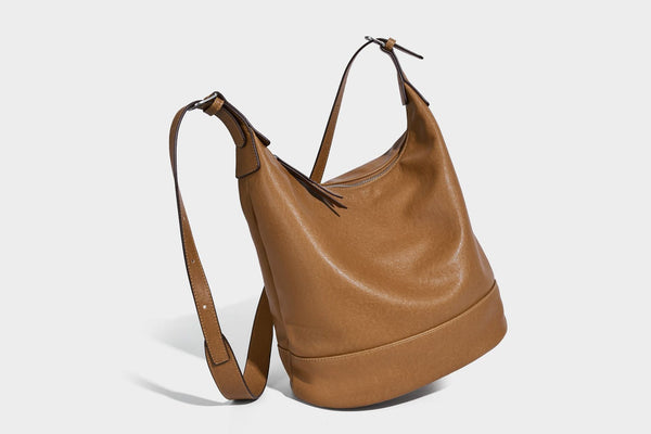 Slouchy bucket hobo shoulder bag in dark brown with glossy leather-look finish, top zip closure, and long adjustable, detail