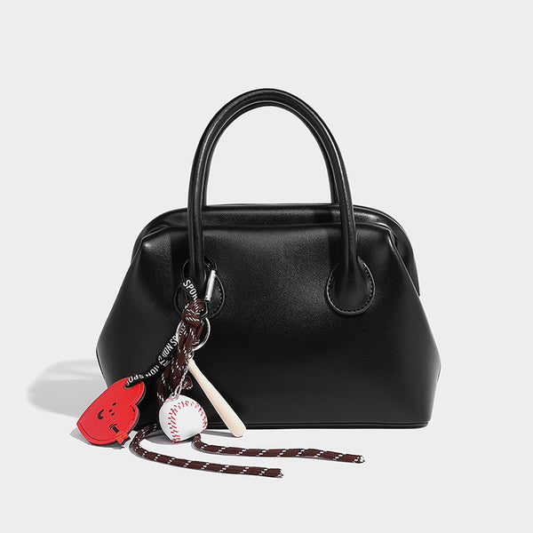 Small structured shell top-handle bag in red with heart charm and braided cord detail, smooth leather-look finish, detail