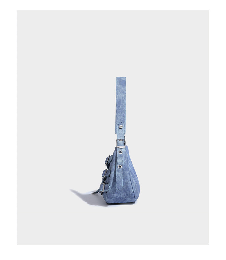 Crescent shoulder bag in washed blue denim-look PU with stacked buckle straps, front zip pocket, and silver-tone hardware