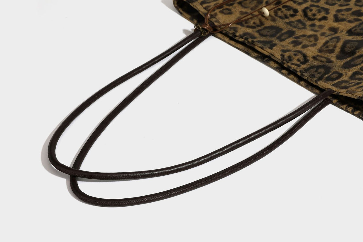 Large leopard print shoulder tote bag in tan and brown with slim dark straps and dangling beaded charm hardware, detail view