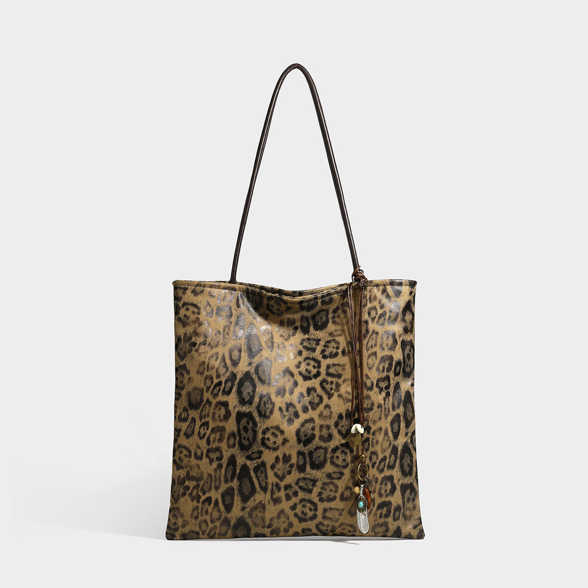 Large leopard print shoulder tote bag in tan and brown with slim dark straps and dangling beaded charm hardware, detail view