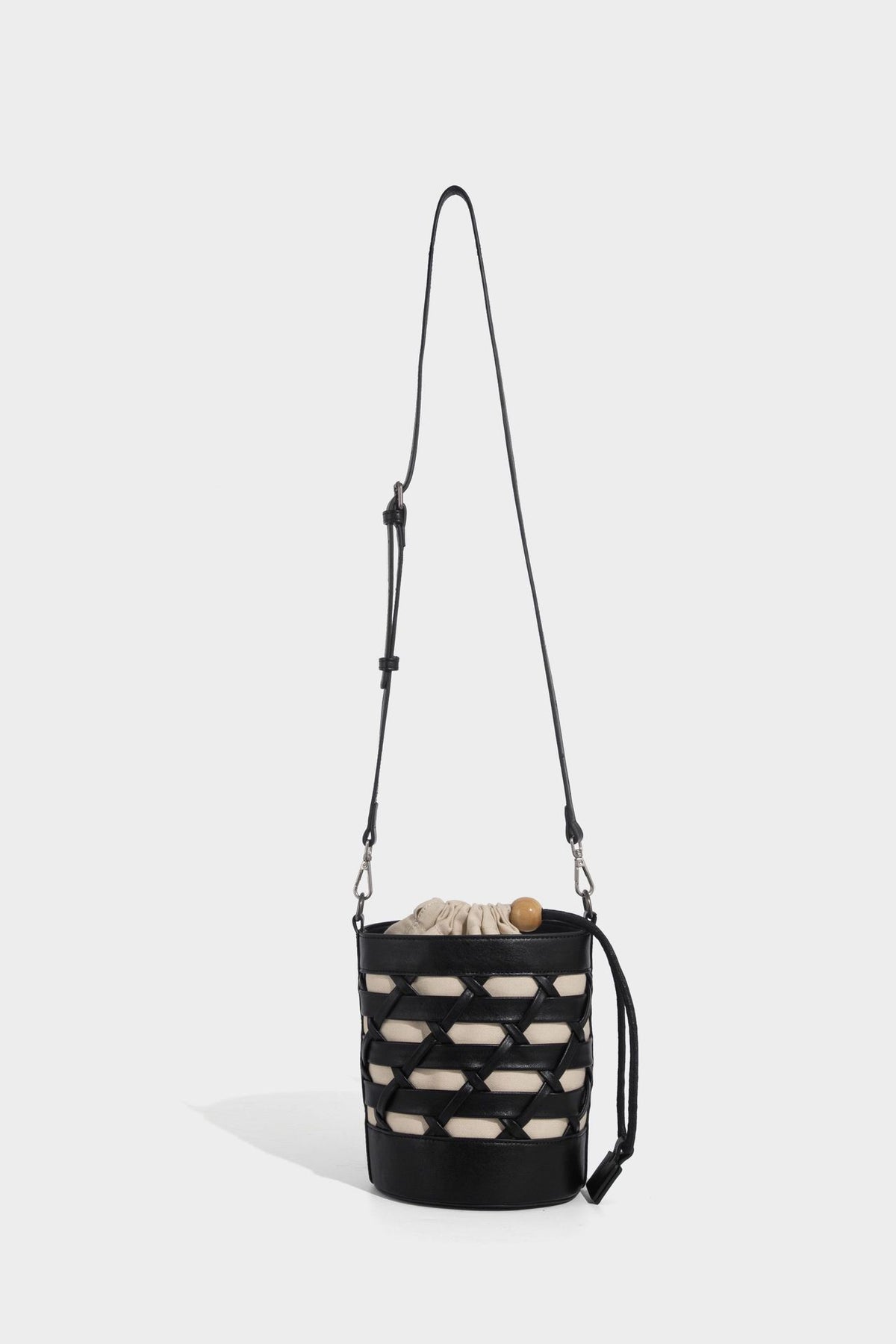 Small cylindrical woven lattice bucket bag with leather-look black trim, beige canvas body, wooden bead drawstring closure