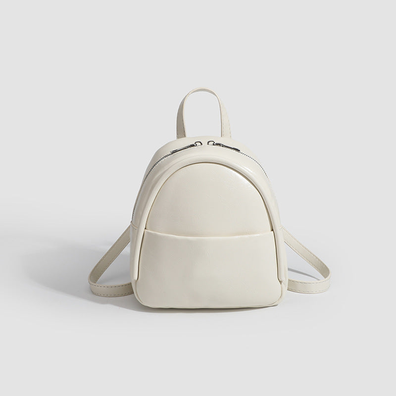 Kompakter, abgerundeter Mini-Rucksack im Lederlook mit glänzender Oberfläche, Reißverschluss oben, Vordertasche und Tragegriff oben, Detailansicht