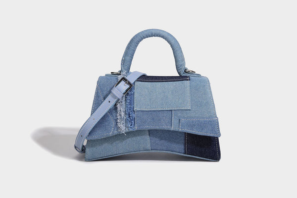 Structured patchwork denim trapezoid satchel bag with frayed panel trim, rounded top handle, and silver-tone hardware, detail