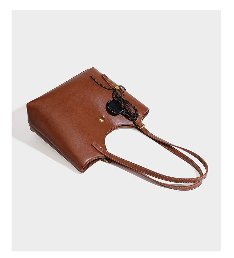 Structured smooth leather-look tote bag with long shoulder strap, gold-tone hardware, and hanging tassel-coin charm, detail