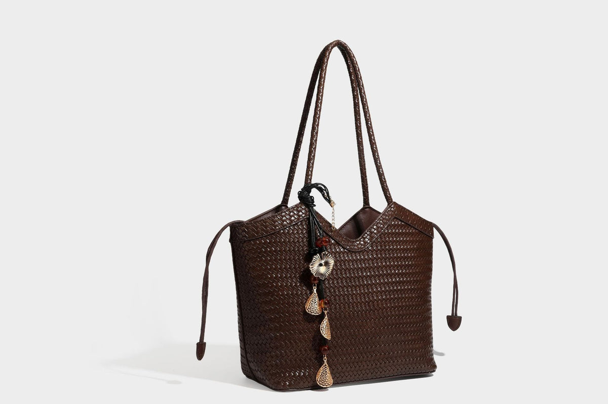 Olivgrüne Tote-Bag in Korbgeflecht-Optik mit dunkelbraunen geflochtenen Schulterriemen, seitlichen Kordelzügen und Perlenanhänger in Goldoptik