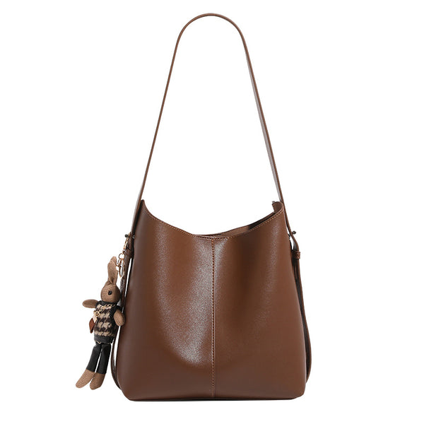 Smooth leather-look bucket bag with long flat shoulder strap, open top, gold-tone hardware, and decorative rabbit charm