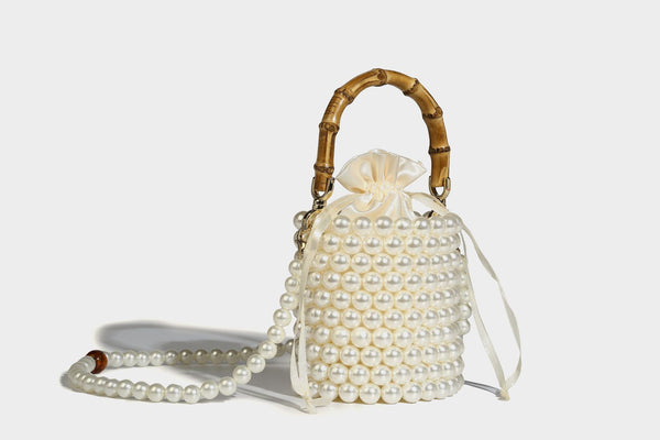 Small cylindrical bucket bag with glossy faux-pearl bead exterior, bamboo arched top handle, satin drawstring closure, and