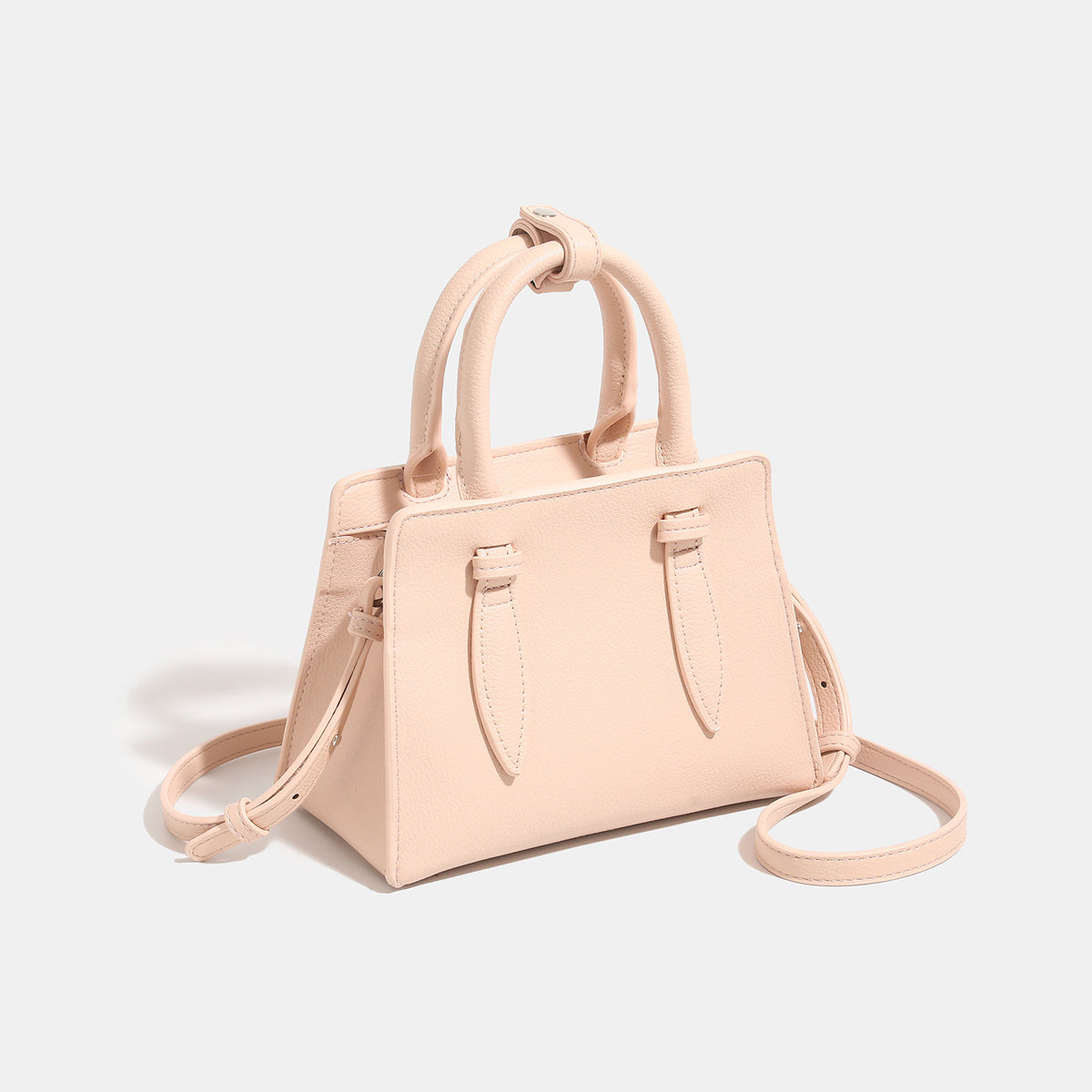 Small structured trapezoid top-handle bag in pebbled matte finish with decorative strap tabs, twin knotted handles, and