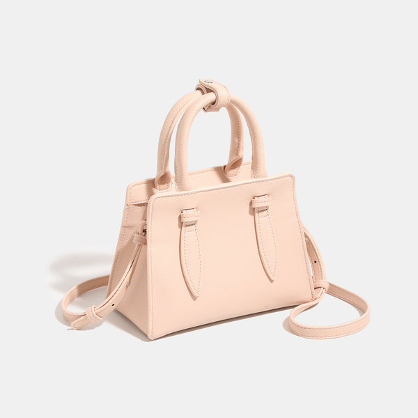 Small structured trapezoid top-handle bag in pebbled matte finish with decorative strap tabs, twin knotted handles, and