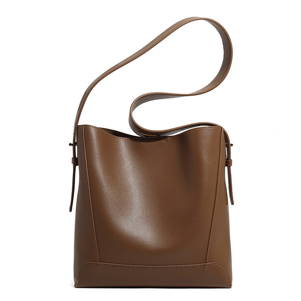 Structured smooth leather-look bucket shoulder bag with long adjustable strap and gold-tone buckle hardware in brown, detail