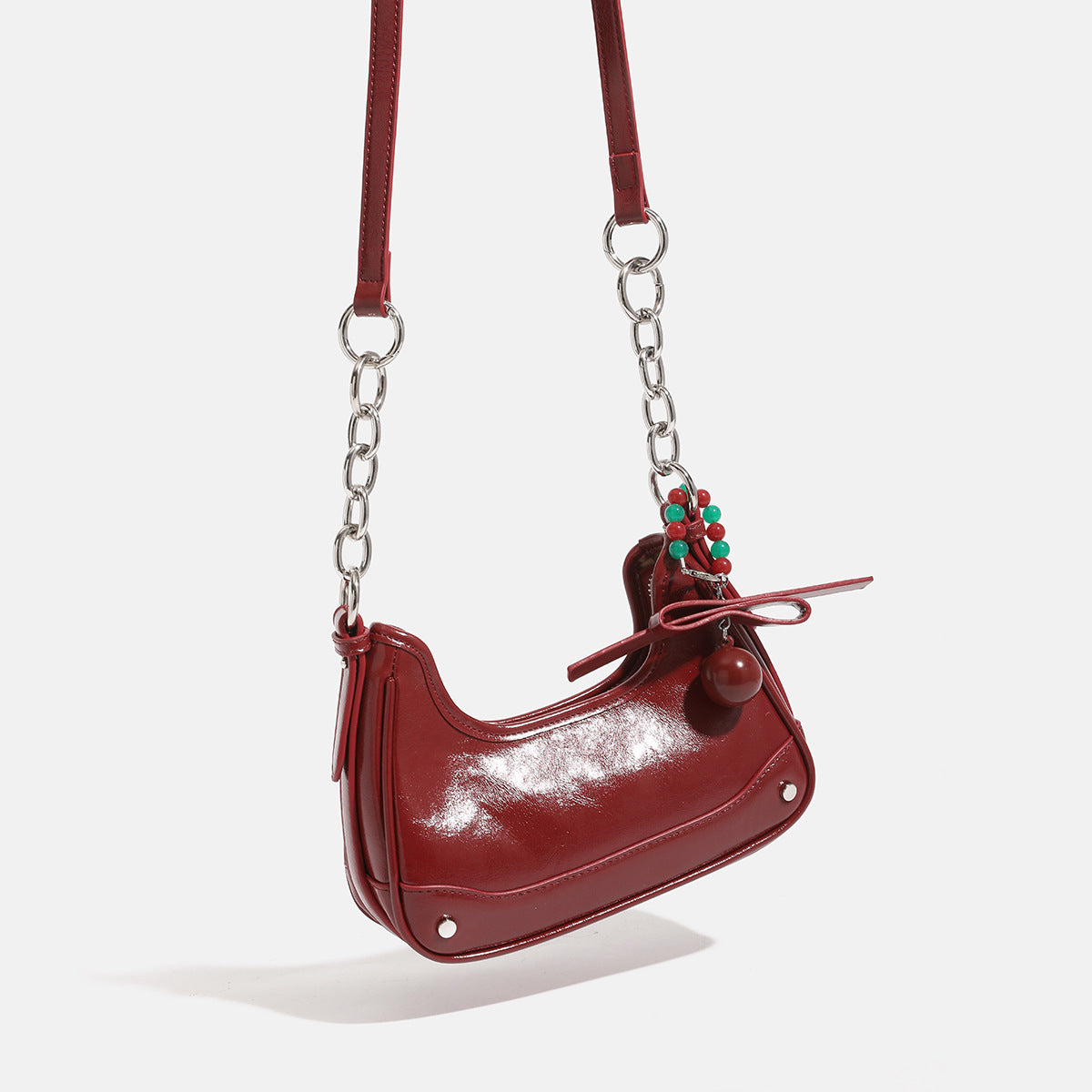 Kompakte Hobo-Schultertasche in Halbmondform mit glänzender bordeauxroter Oberfläche in Lederoptik, silberfarbenem Kettenriemen und Quaste aus roten und grünen Perlen