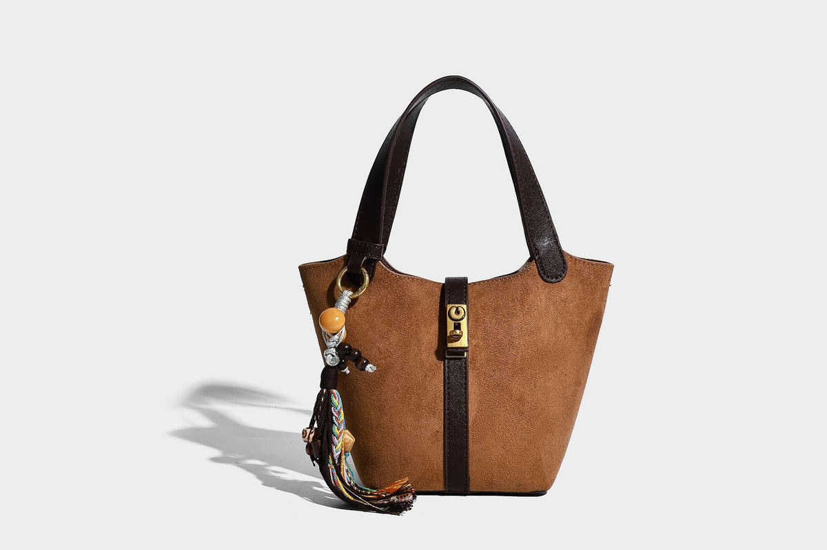 Small structured trapezoid tote bag in matte suede-look finish with black contrast trim, gold-tone front clasp, tassel charm