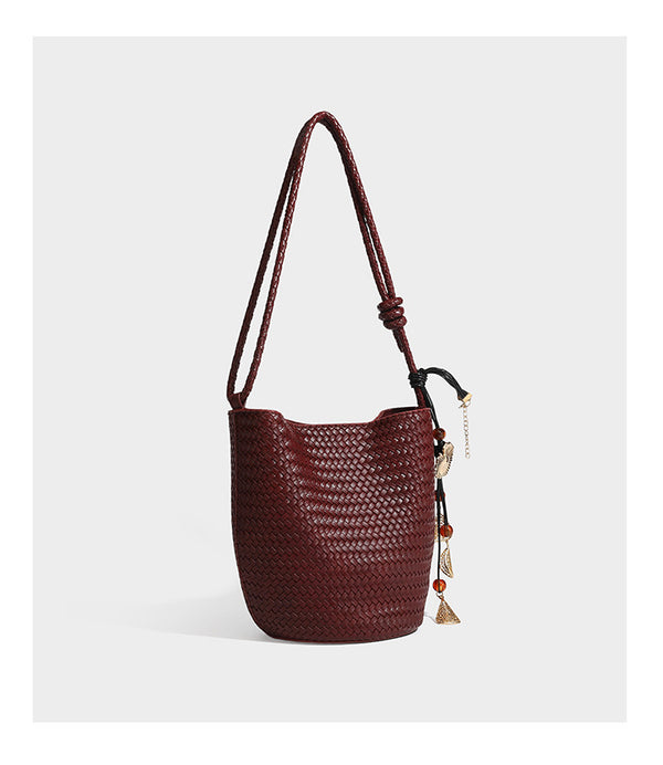 Olive green woven leather-look bucket bag with braided crossbody strap, knotted adjustment, and gold-tone tassel charm with