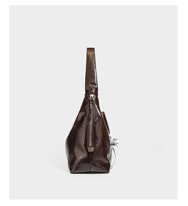 Lässige Hobo-Schultertasche in glänzender Lederoptik mit silbernen Schnürösen und einer Schleife aus Ripsband auf der Vorderseite, Detail