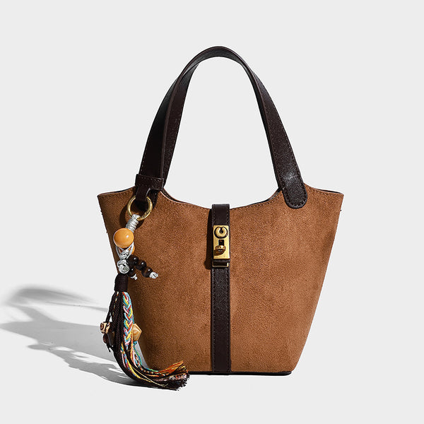Small structured trapezoid tote bag in matte suede-look finish with black contrast trim, gold-tone front clasp, tassel charm