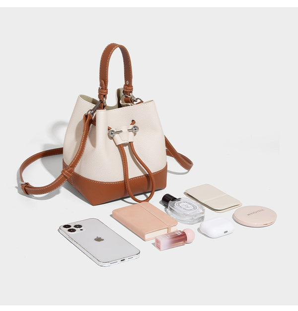 Small two-tone pebbled drawstring bucket bag with tan contrast base, metal toggle hardware, short top handle, and detachable
