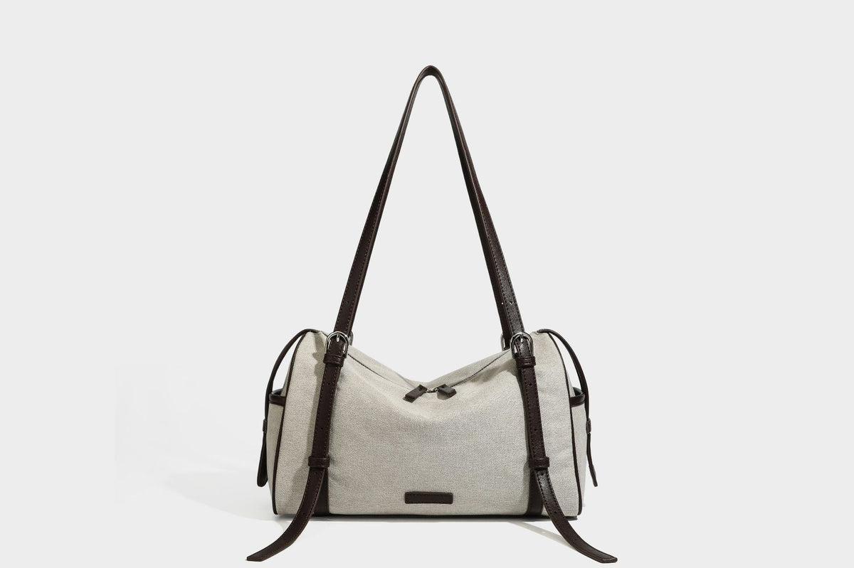 Beige canvas barrel bag with dark brown leather-look trim, silver-tone hardware, top zip closure, and adjustable shoulder