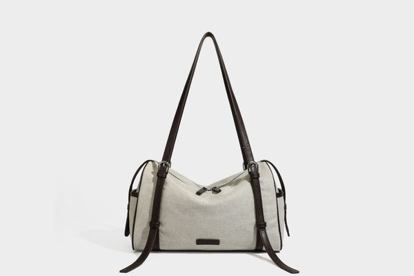 Beige canvas barrel bag with dark brown leather-look trim, silver-tone hardware, top zip closure, and adjustable shoulder
