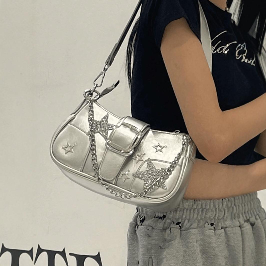 Kompakte Schultertasche in Metallic-Silber mit glitzernden Sternapplikationen, Sternanhängern mit Strasssteinen, vorderem Riemen mit Schnalle und markantem