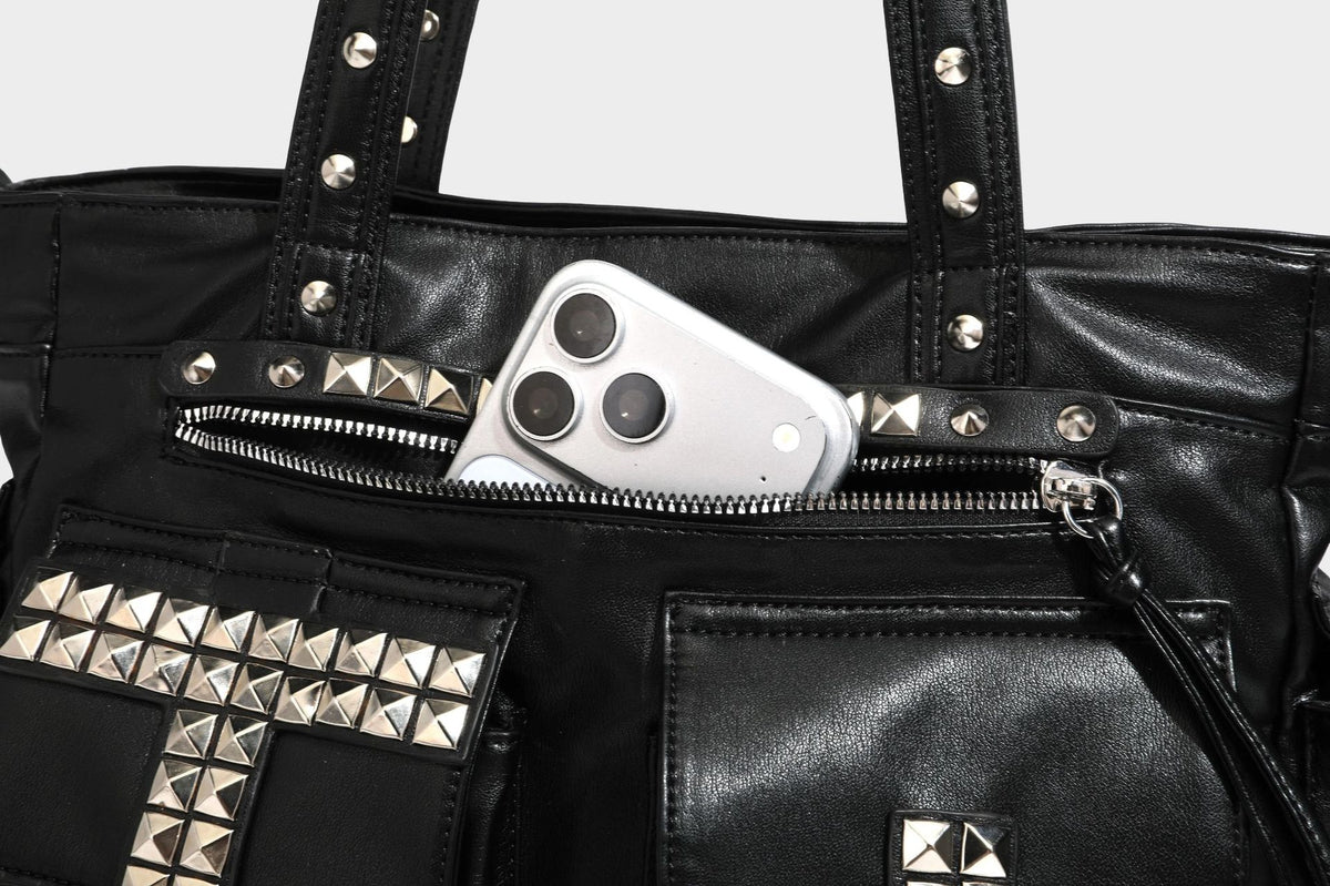 Black leather-look tote bag with silver pyramid studs on handles and front panel, multiple flap and zip exterior pockets