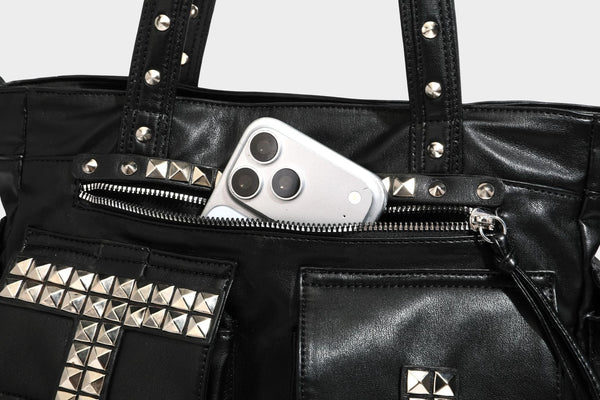 Black leather-look tote bag with silver pyramid studs on handles and front panel, multiple flap and zip exterior pockets