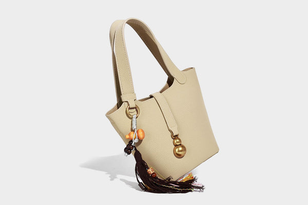 Kleine matte Beuteltasche mit genarbter Oberfläche, antikgoldfarbenen Ringbeschlägen, Perlen- und Quastenanhänger, kurzen Tragegriffen oben und