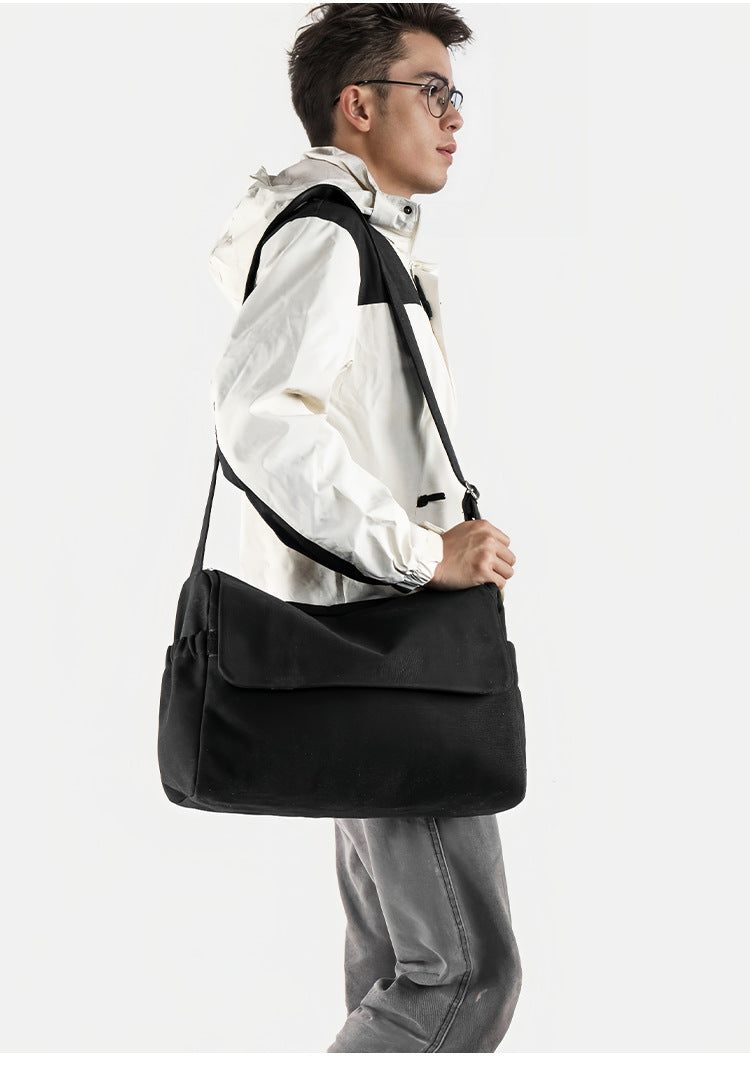 Große schwarze Messenger-Tasche aus mattem Canvas mit Überschlag vorn, Reißverschluss oben, elastischen Seitentaschen und verstellbarem silberfarbenem