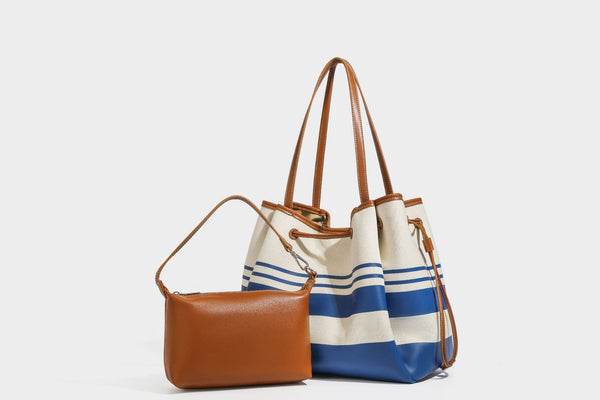Large cream and navy striped canvas bucket tote bag with tan leather-look trim, drawstring closure, and double shoulder