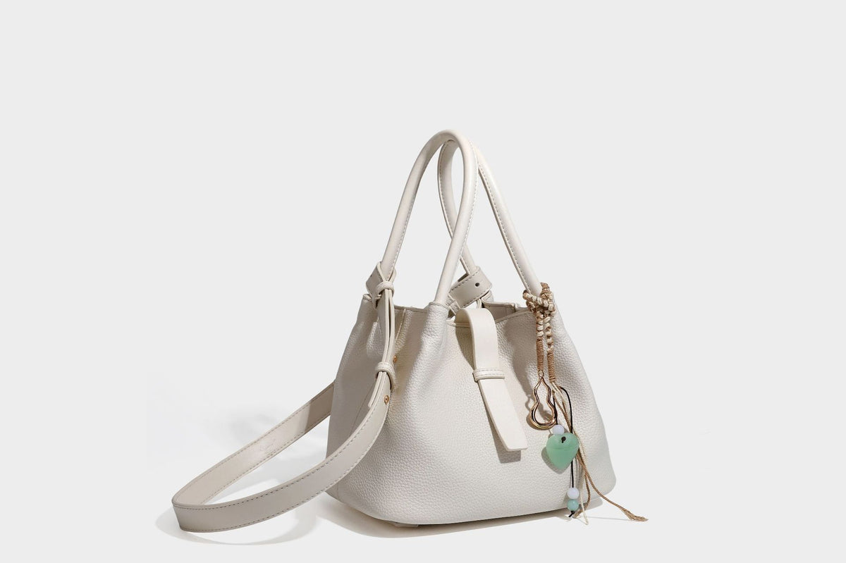 Pebbled leather-look bucket tote bag with rolled double handles, drawstring closure, braided cord charm, and detachable