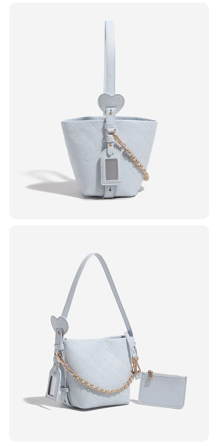 Small diamond-quilted bucket bag with gold-tone chain accent, heart strap detail, hanging tag, and matching zip coin pouch
