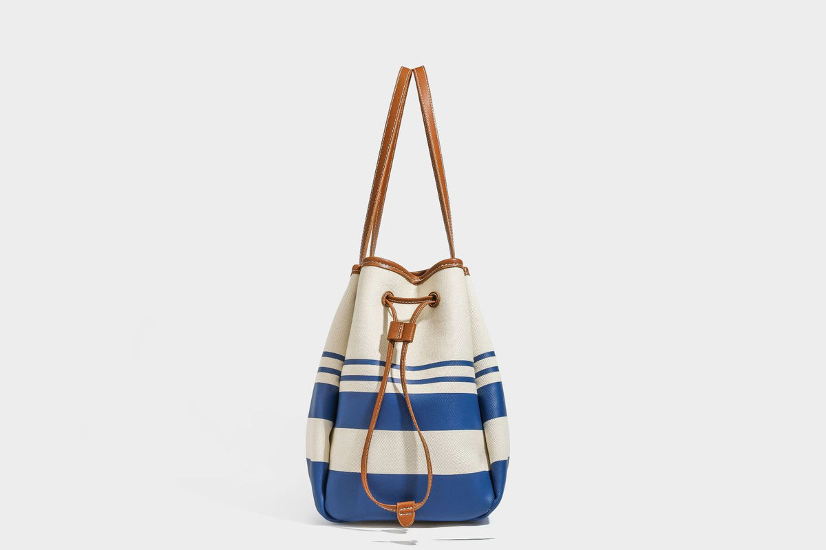Large cream and navy striped canvas bucket tote bag with tan leather-look trim, drawstring closure, and double shoulder