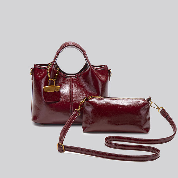 Structured crinkle-gloss top-handle satchel in deep burgundy with antique gold lock charm and detachable shoulder strap