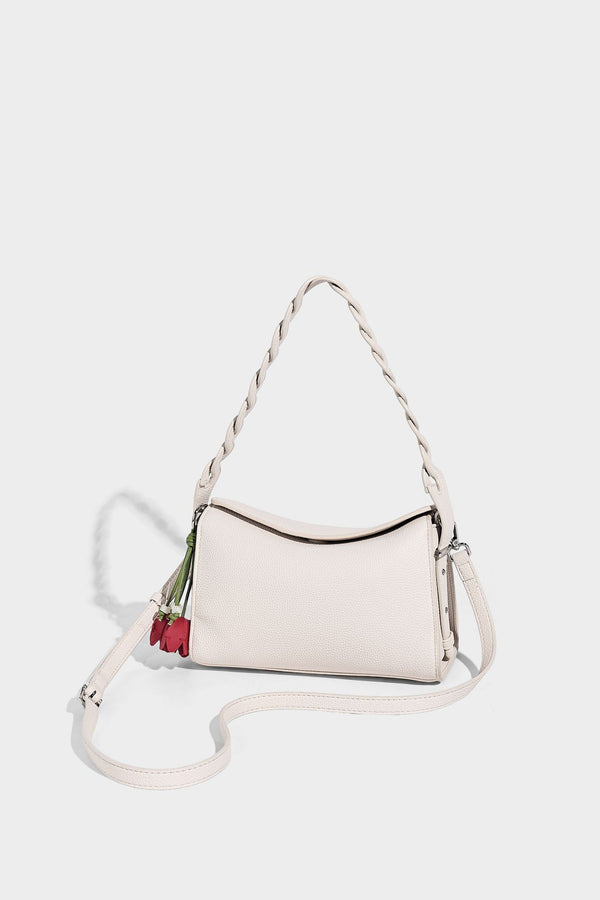 Small structured pebbled-finish shoulder bag with braided top handle, detachable crossbody strap, floral tassel charm, and