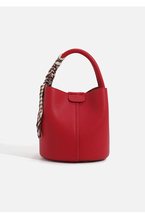 Pebbled leather-look bucket bag with checkered scarf-wrapped top handle, flap tab closure, gold-tone hardware, and matching