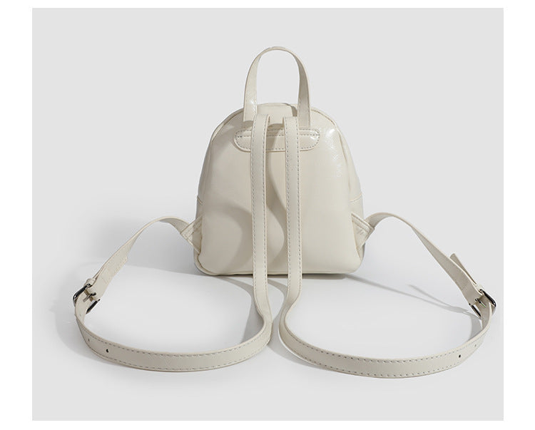 Kompakte, abgerundete Mini-Rucksackhandtasche mit glänzender Lederoptik, Reißverschluss oben, Fronttasche, Tragegriff oben und Detailansicht