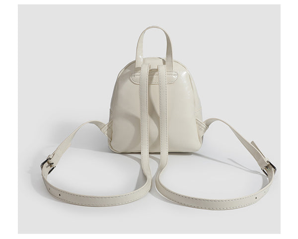 Kompakte, abgerundete Mini-Rucksackhandtasche mit glänzender Lederoptik, Reißverschluss oben, Fronttasche, Tragegriff oben und Detailansicht