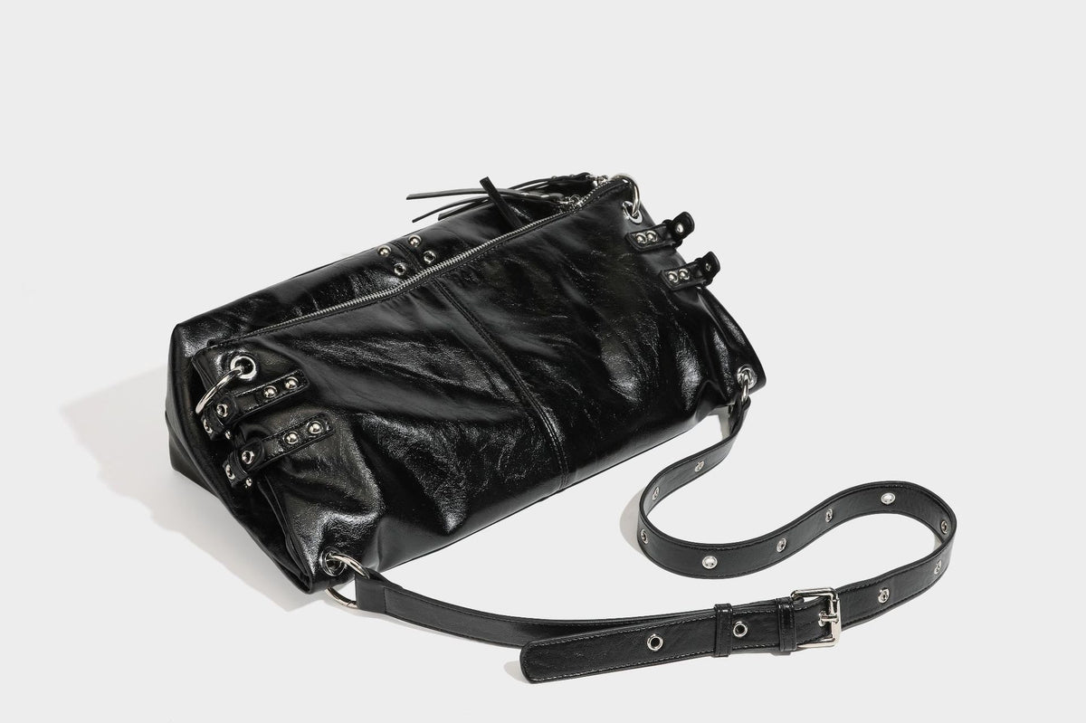 Black glossy leather-look slouchy shoulder bag with silver stud and eyelet hardware, top zip closure, front zip pocket, and