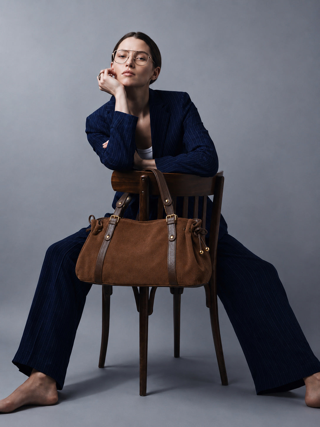 Soft suede-texture shoulder bag in brown with drawstring sides, leather-look vertical straps, gold-tone buckle hardware, and