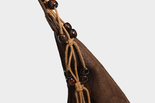 Slouchy boho hobo shoulder bag in embossed brown suede-look finish with beaded strap, cord tassels, and brass-tone leaf